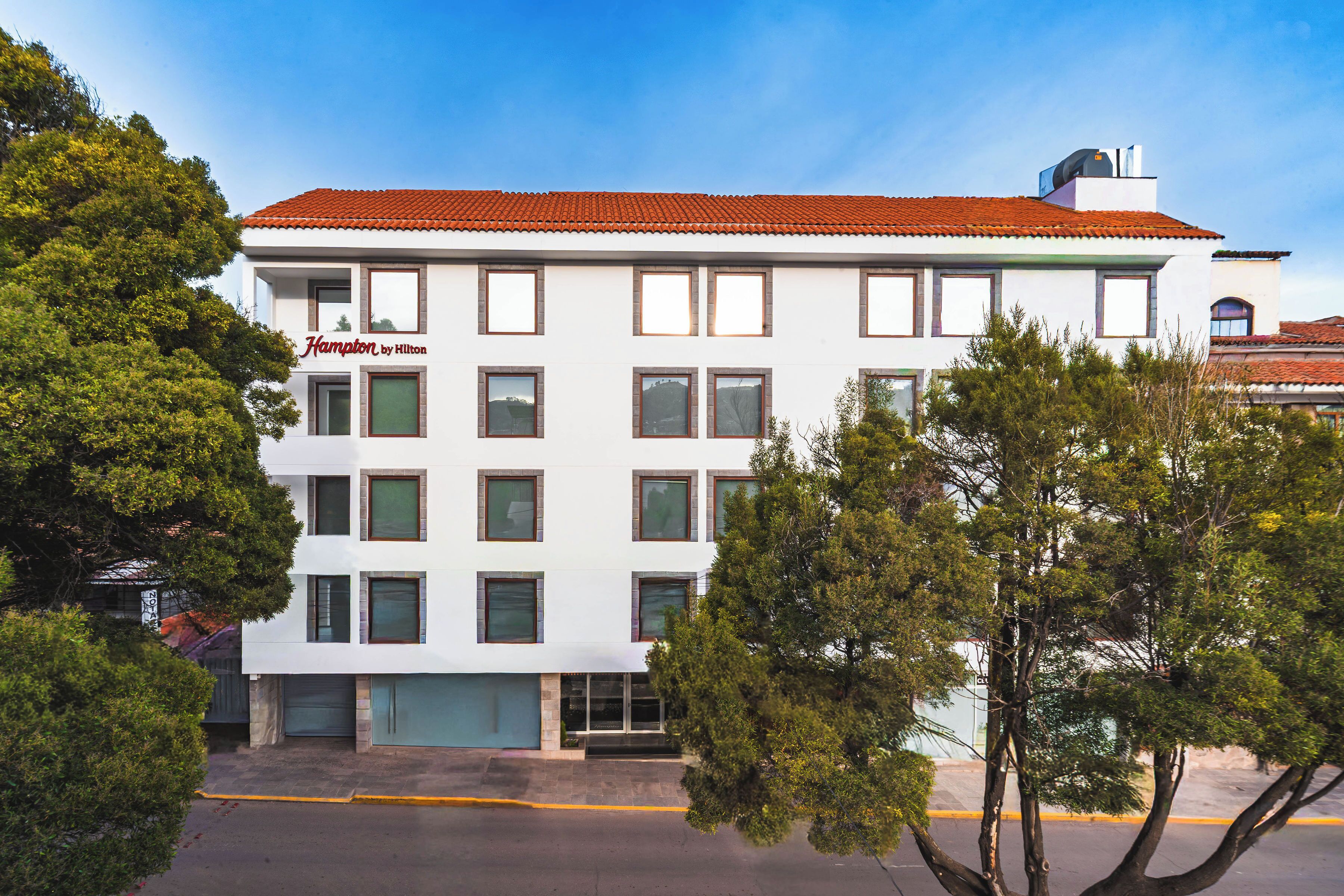 A white building with a red roof, multiple windows, and a sign reading "Hampton by Hilton".