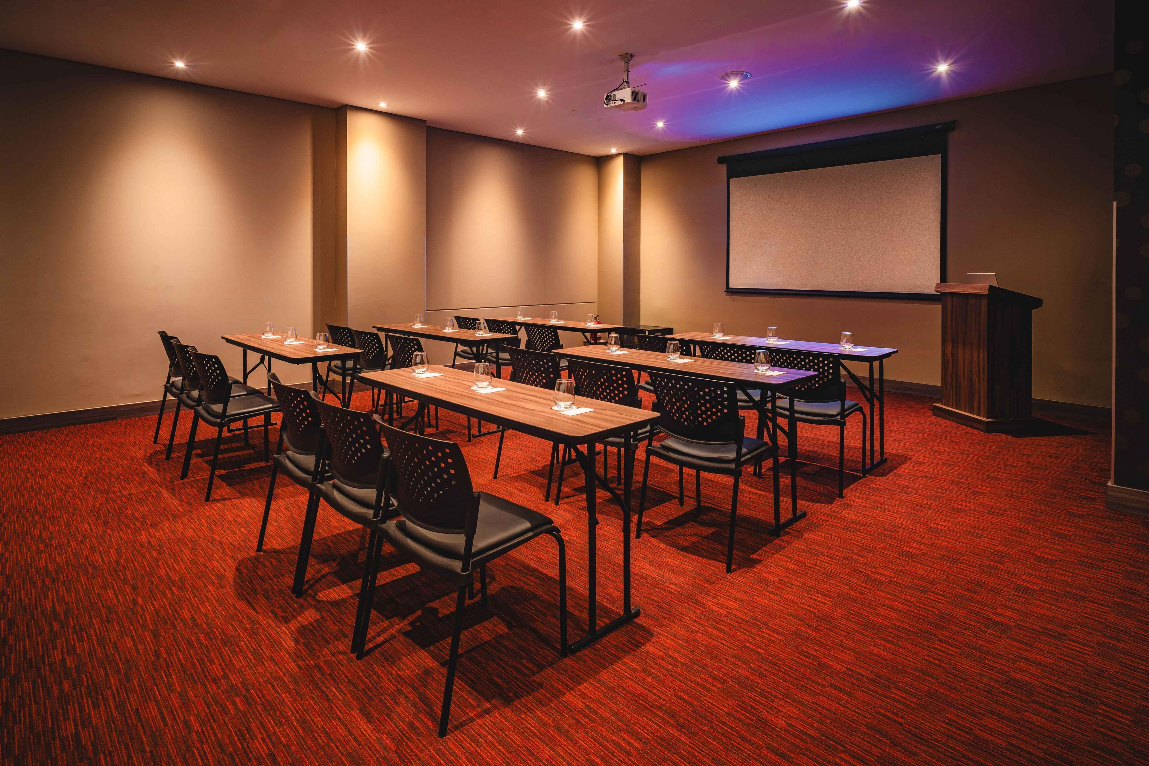 A conference room with multiple tables and chairs, a projector screen, and a podium.