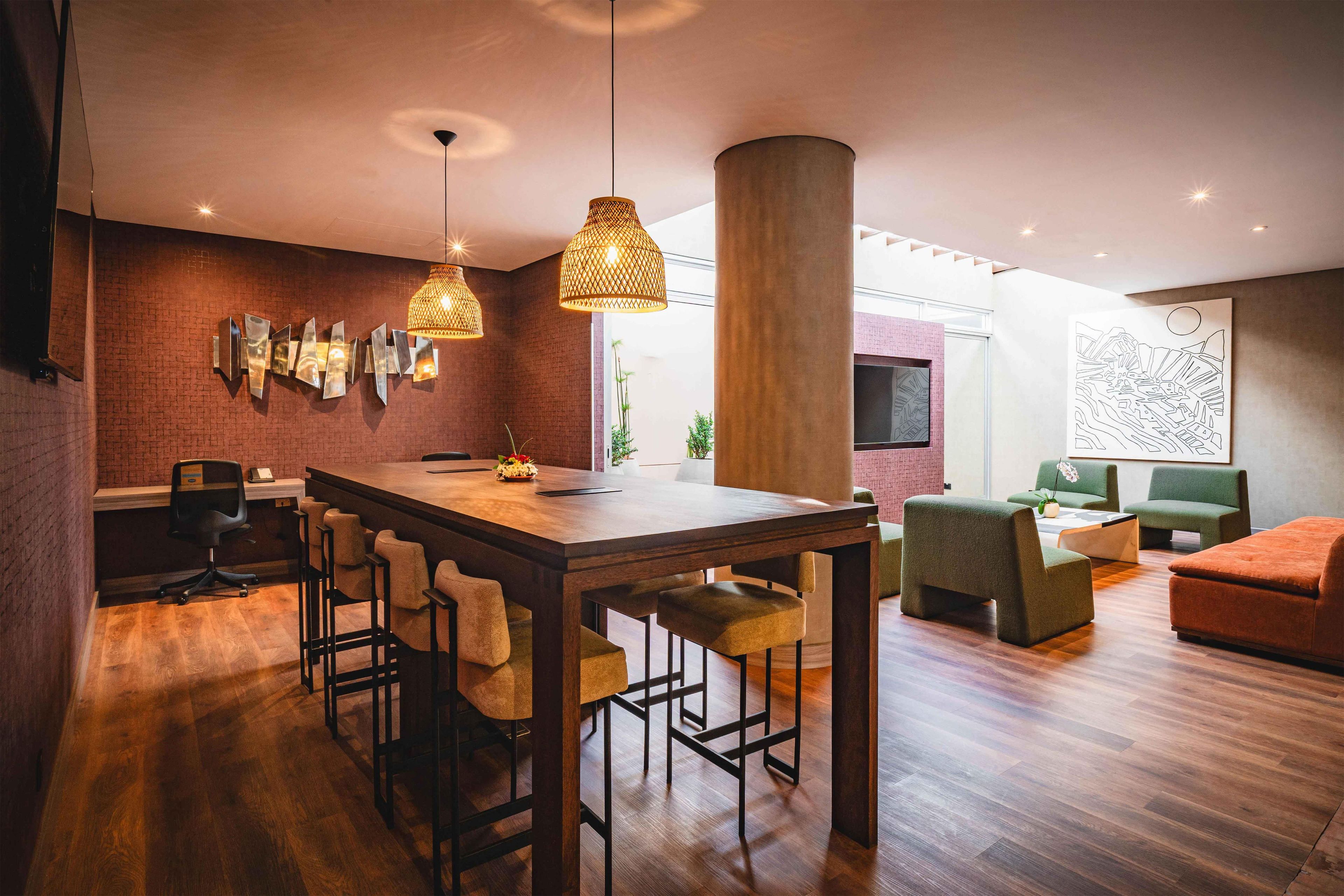 Un intérieur moderne avec une table à manger en bois, des tabourets de bar et un coin salon agrémenté de canapés verts et orange.