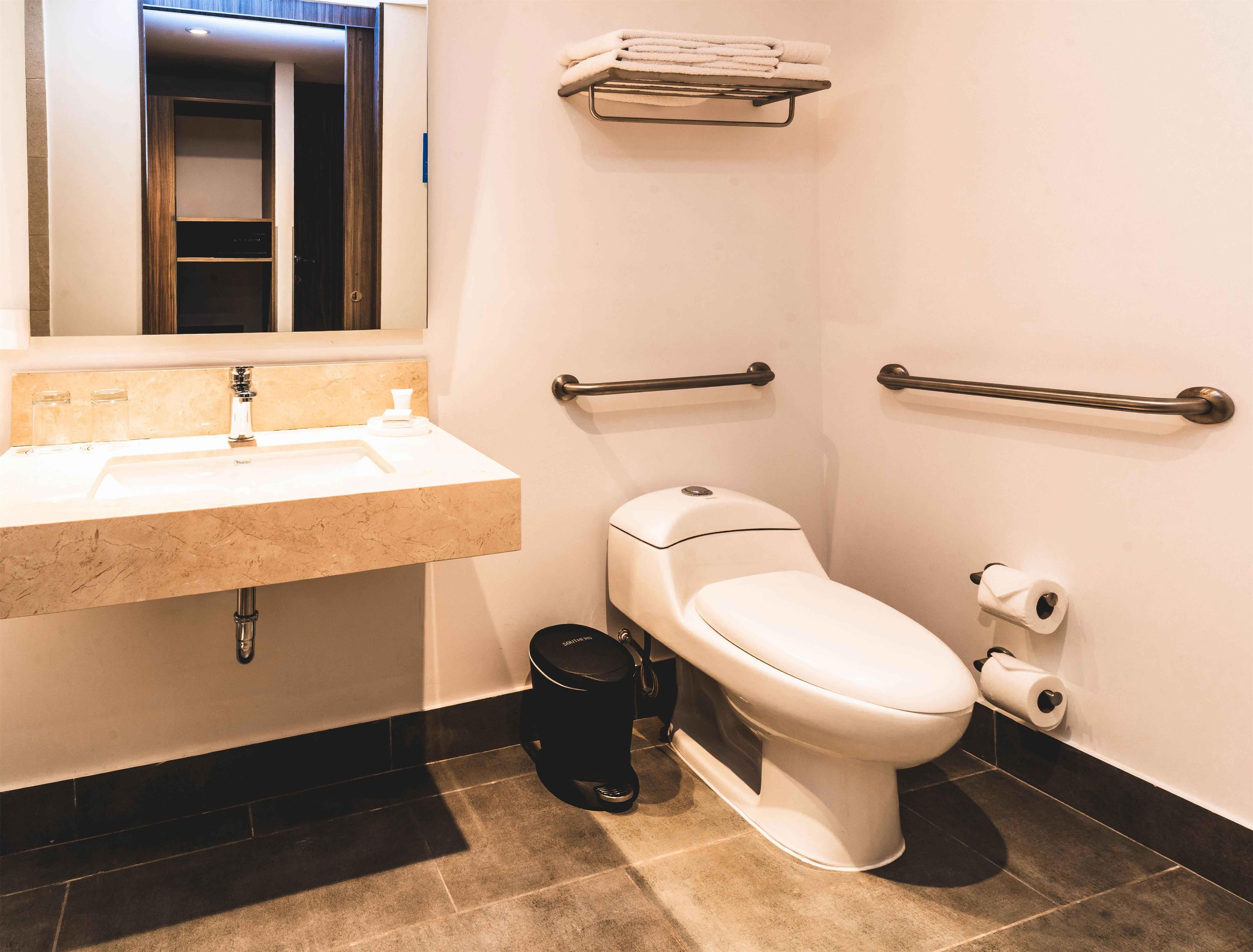 Un baño moderno con lavamanos, inodoro y barras de apoyo.