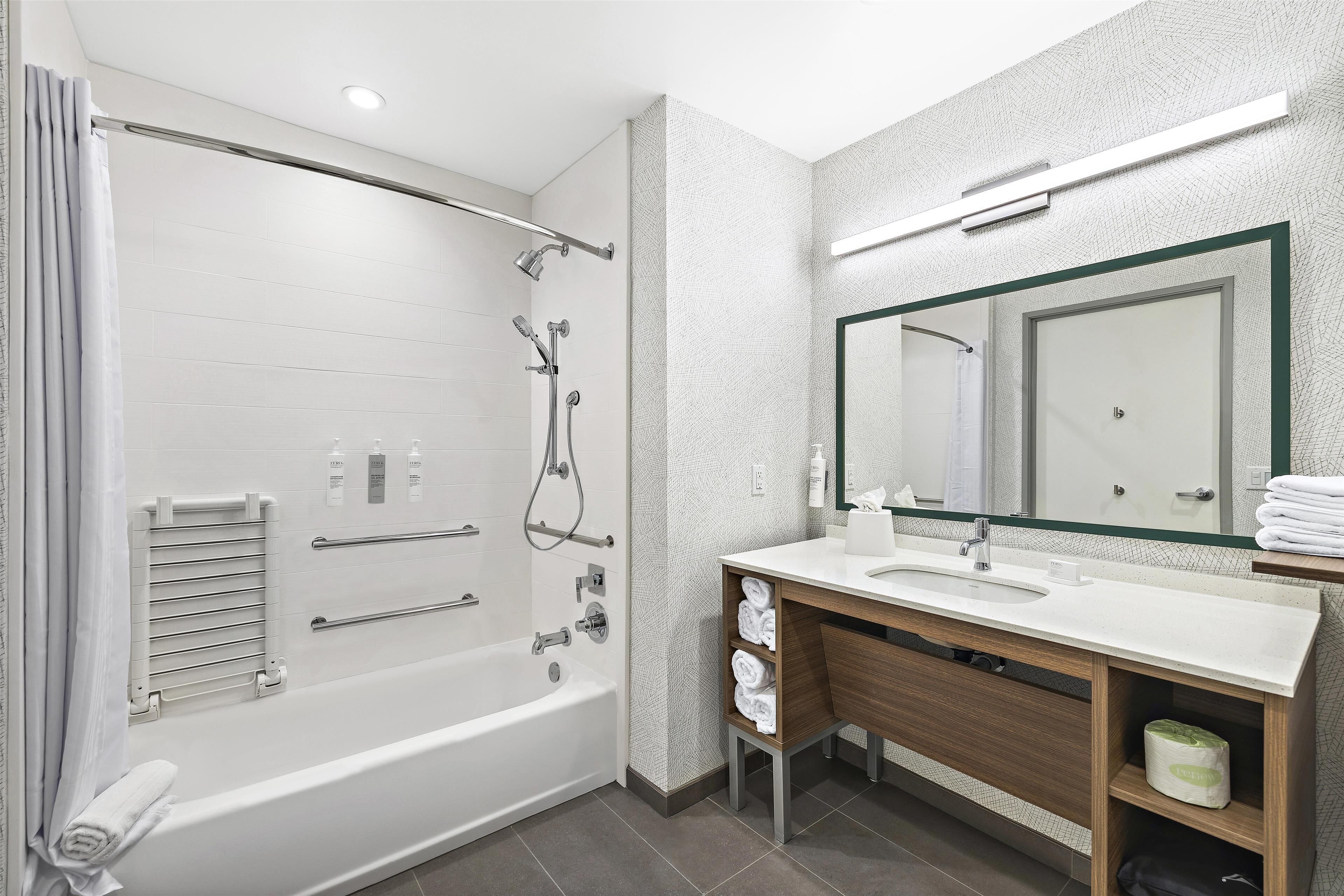 A modern bathroom with a bathtub, shower, vanity, and a large mirror.