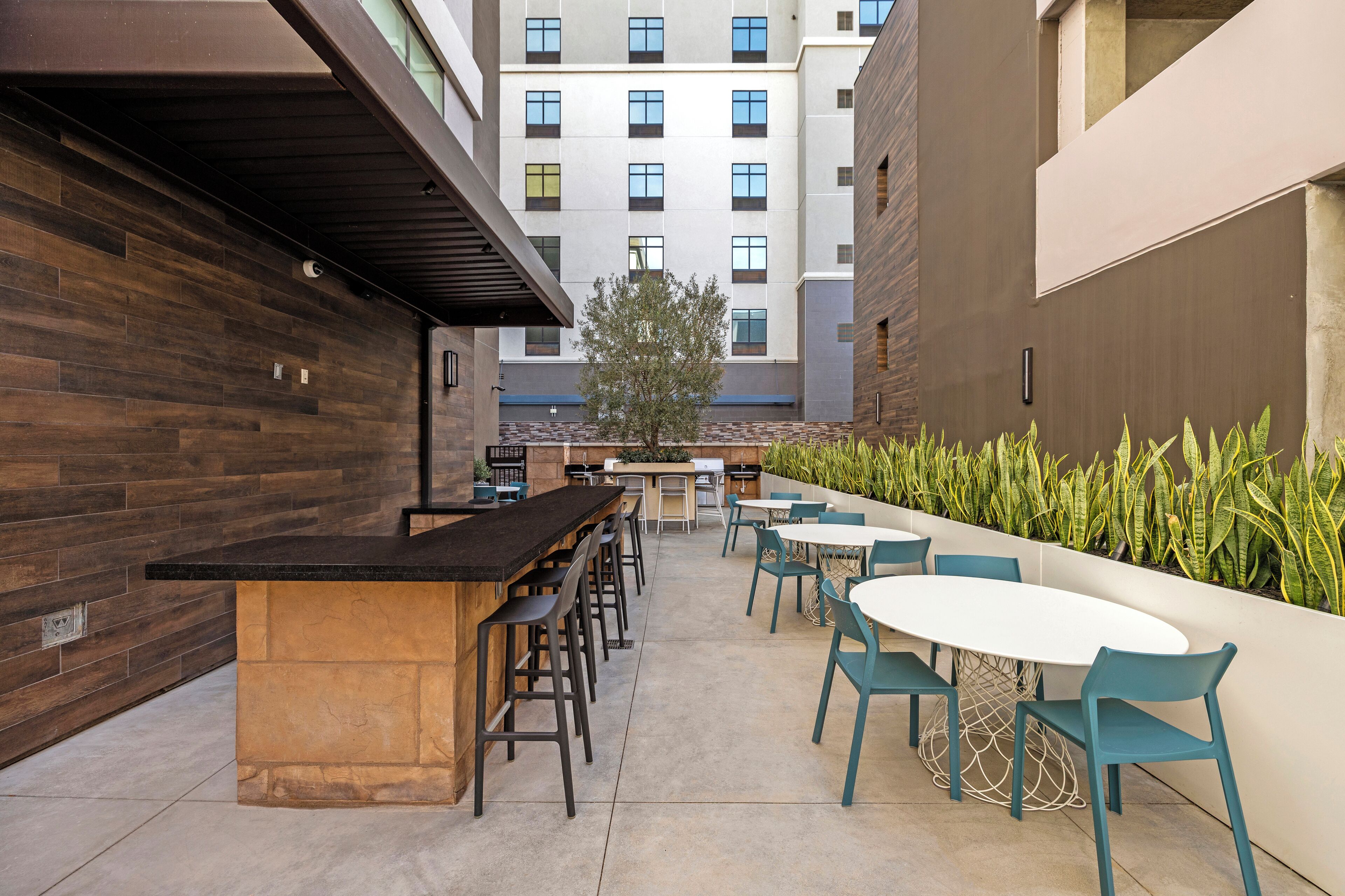 Une terrasse extérieure avec un espace bar, des sièges et une vue sur le bâtiment en arrière-plan.