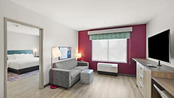 A hotel room with a bed, a sofa, a TV, a desk, and a window with blinds.