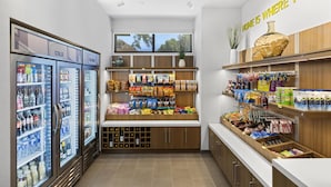 A well-lit store with refrigerated sections, shelves stocked with snacks, and a clear view of the sky through the window. - Home2 Suites by Hilton Riverside Downtown Convention Center (Riverside)
