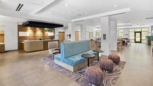 A modern hotel lobby with a reception desk, seating area, and a view of the dining area. - Home2 Suites by Hilton Riverside Downtown Convention Center (Riverside)