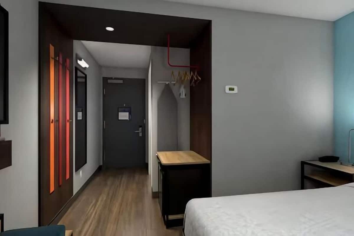 Una habitación de hotel con cama, escritorio, silla, armario y puerta.