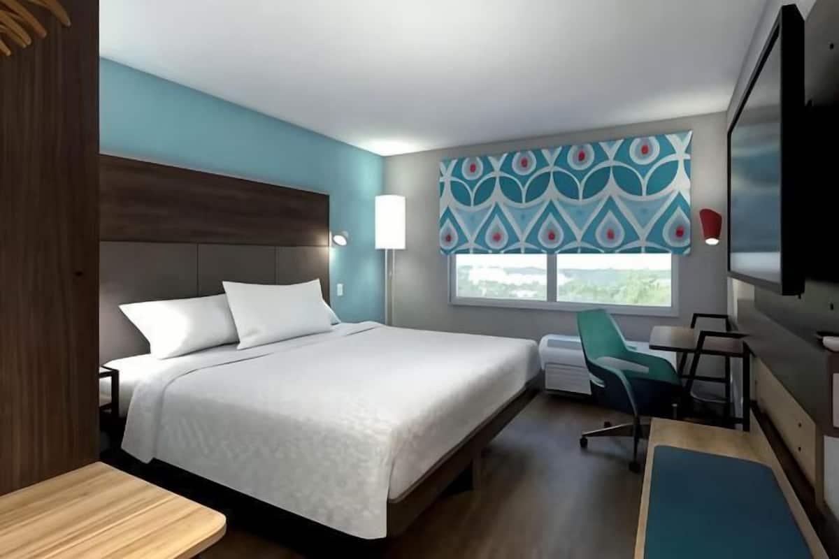 Una habitación de hotel moderna con una cama grande, un escritorio, una silla y un televisor.