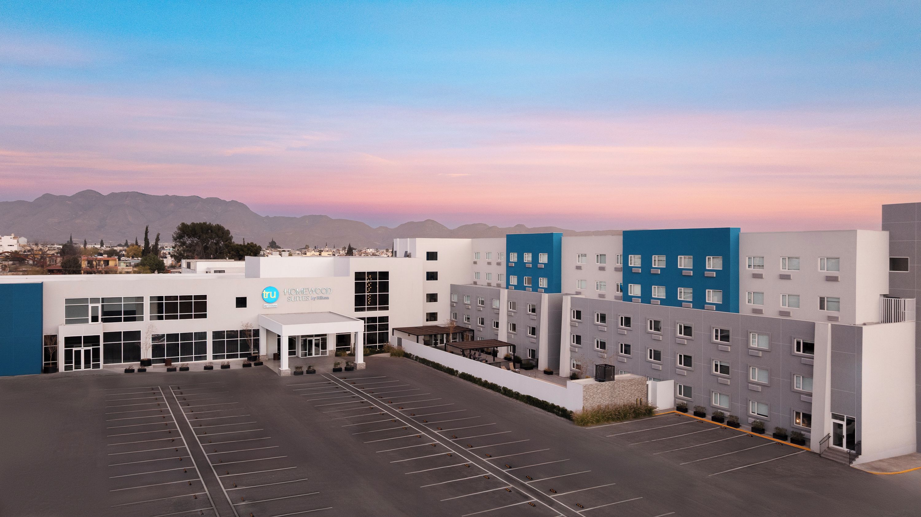A hotel with a modern design, a parking lot, and a mountainous backdrop.