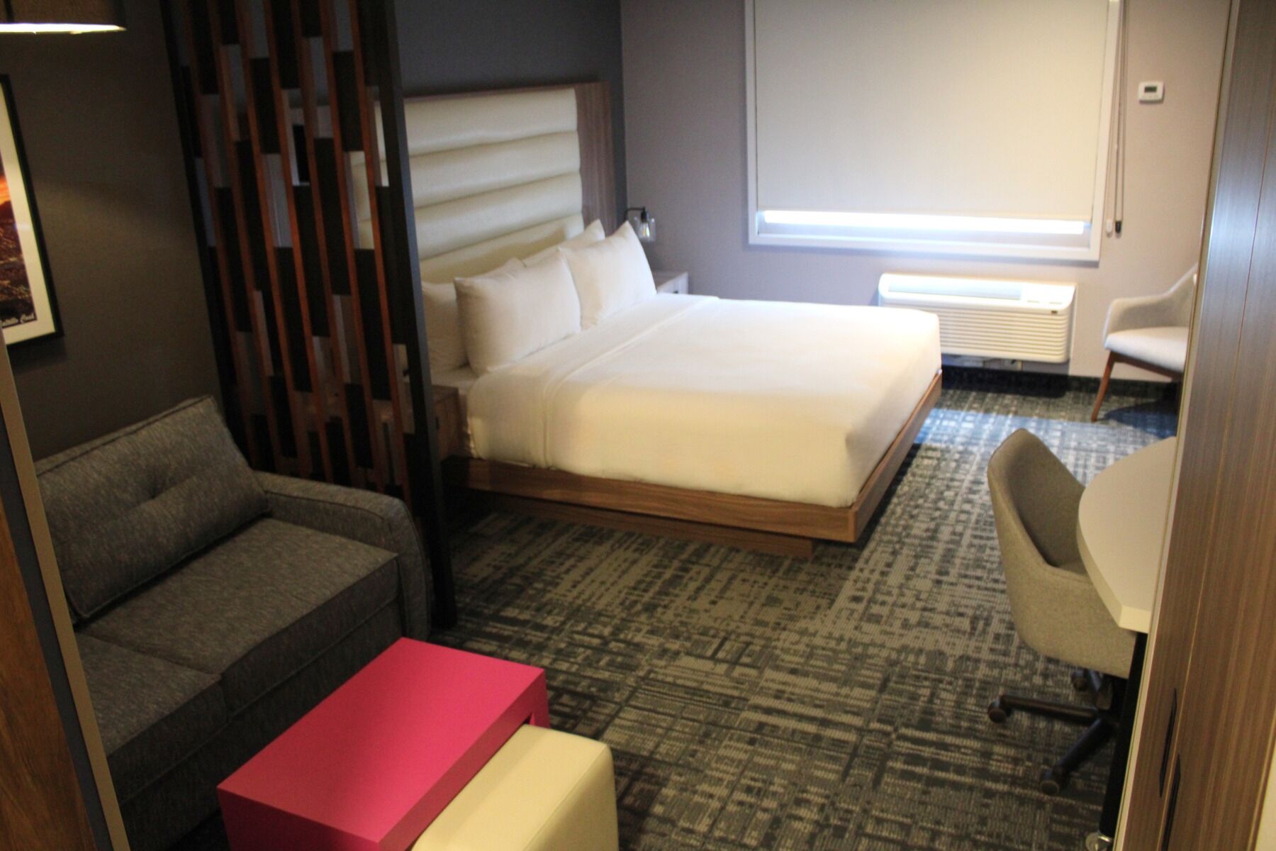 A hotel room with a bed, a sofa, a small table, a chair, and a window with a view.
