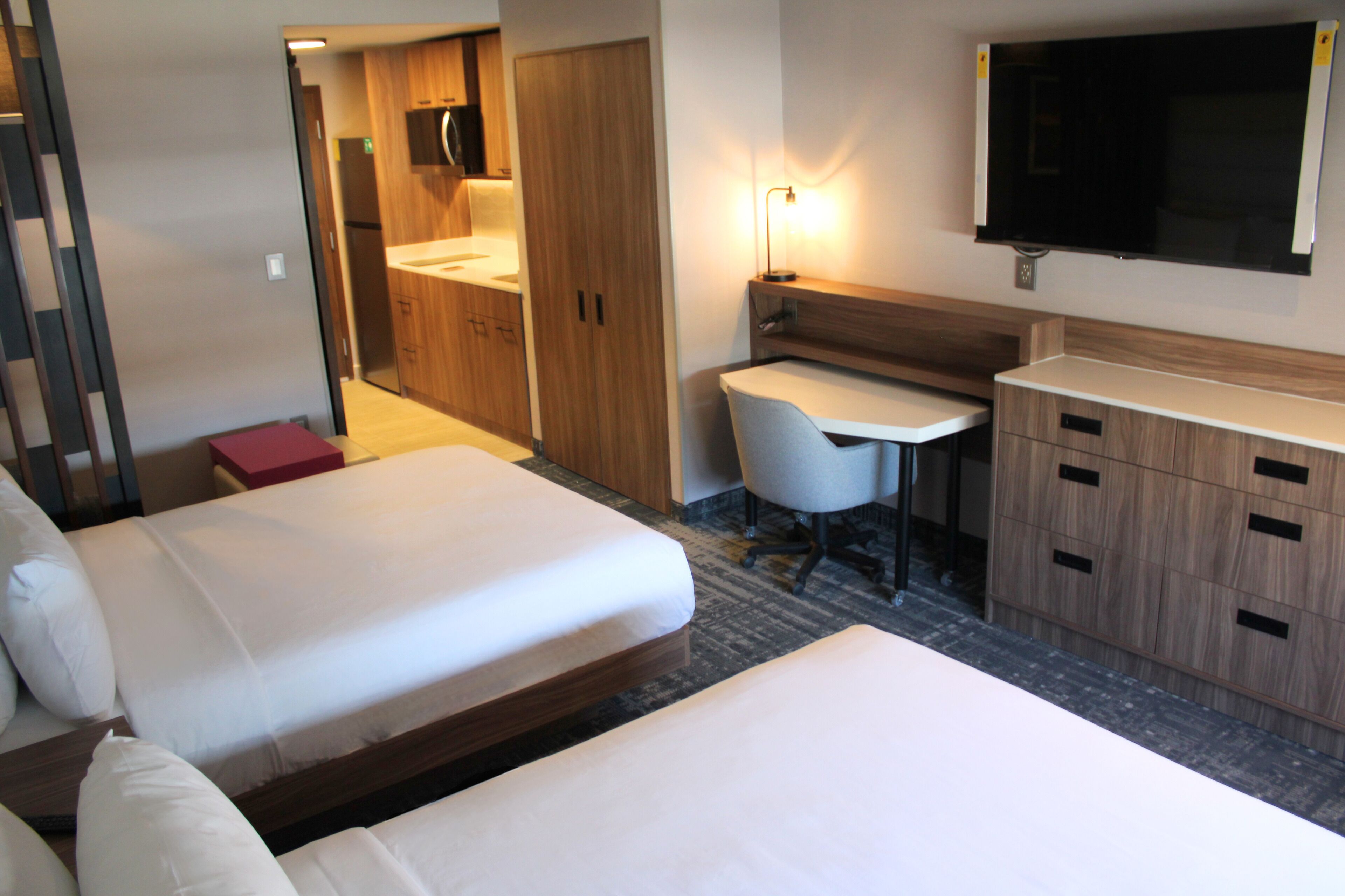 A hotel room with two beds, a desk, a chair, a TV, and a minibar.