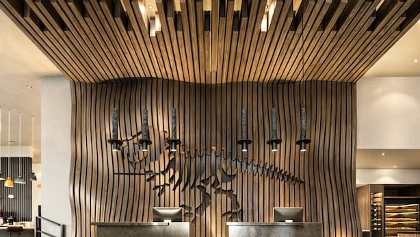 A reception area with a modern design, featuring a wooden wall with vertical slats and a central sculpture. - Homewood Suites By Hilton Saltillo (Saltillo)