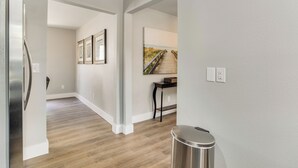 Un couloir doté d’un plancher en bois, d’une poubelle en acier inoxydable et d’une œuvre d’art encadrée accrochée au mur.
