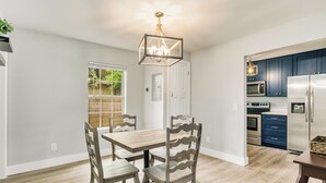 Une cuisine moderne équipée d’appareils électroménagers en acier inoxydable, un coin repas avec une table et des chaises en bois, et un luminaire suspendu.
