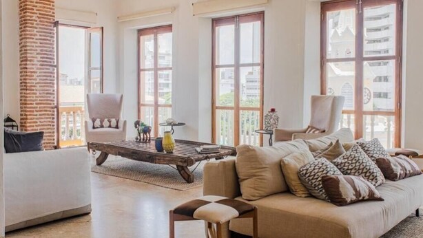 Een ruime woonkamer met een bakstenen zuil, grote ramen, een bank, een salontafel en twee fauteuils.
