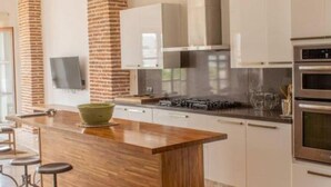Een moderne keuken met een houten keukeneiland, witte kasten en een wand met bakstenen.