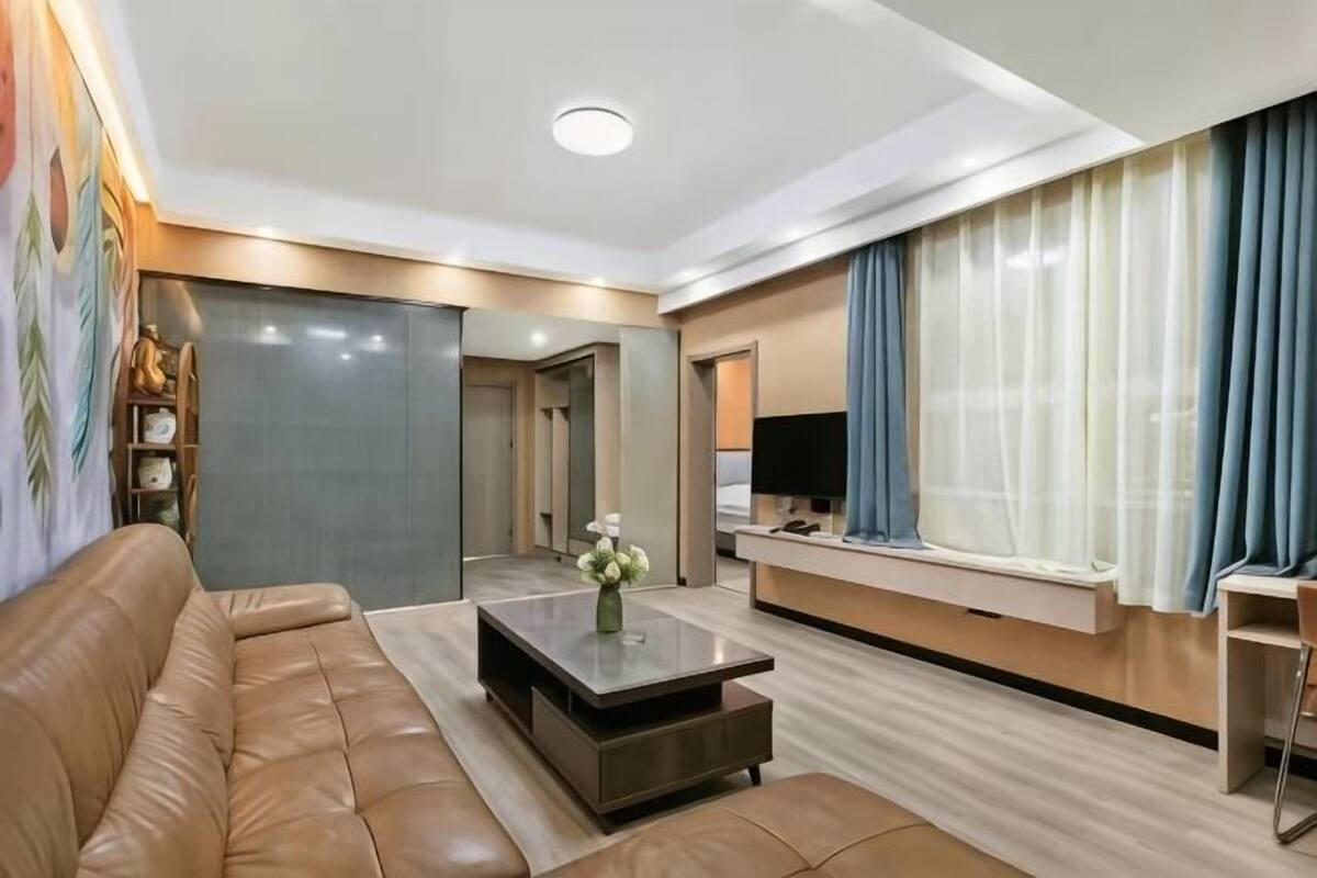 A modern living room with a leather sofa, a coffee table, a flat-screen TV, and a large window with curtains.