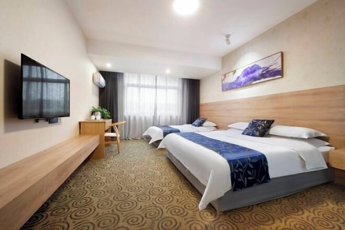 A hotel room with two beds, a TV, a desk, and a window with curtains.