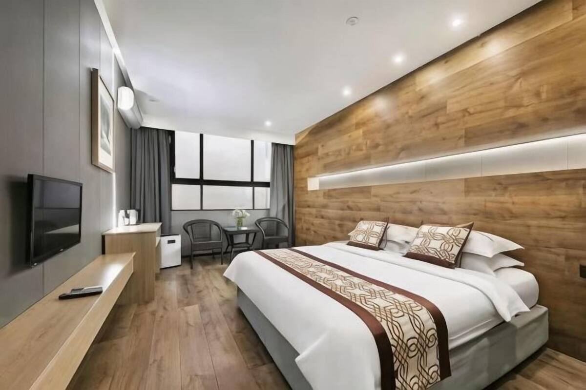 A modern hotel room with a large bed, a desk, a television, and a window with curtains.