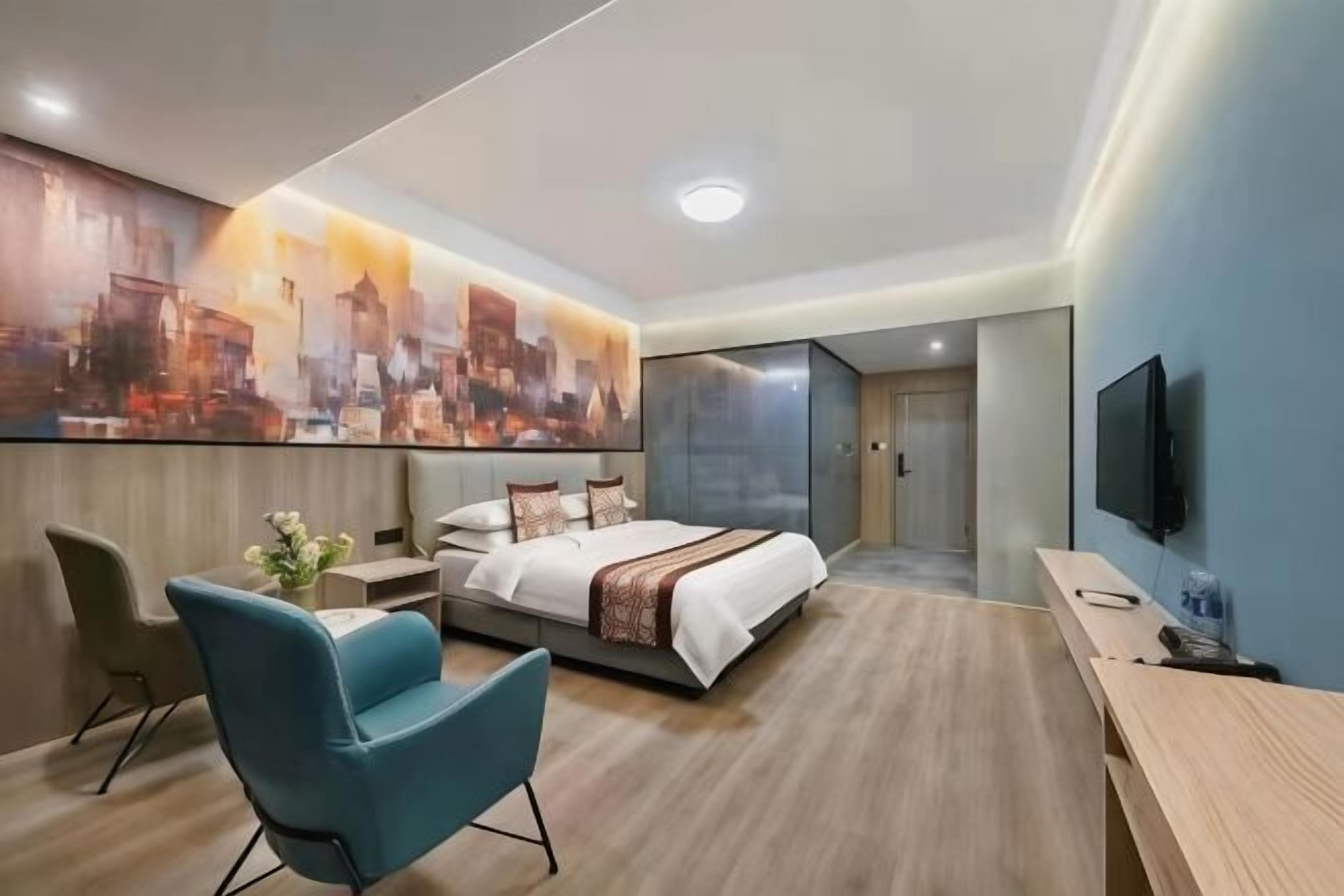 A modern hotel room with a large bed, a desk, a chair, a TV, and a cityscape painting on the wall.