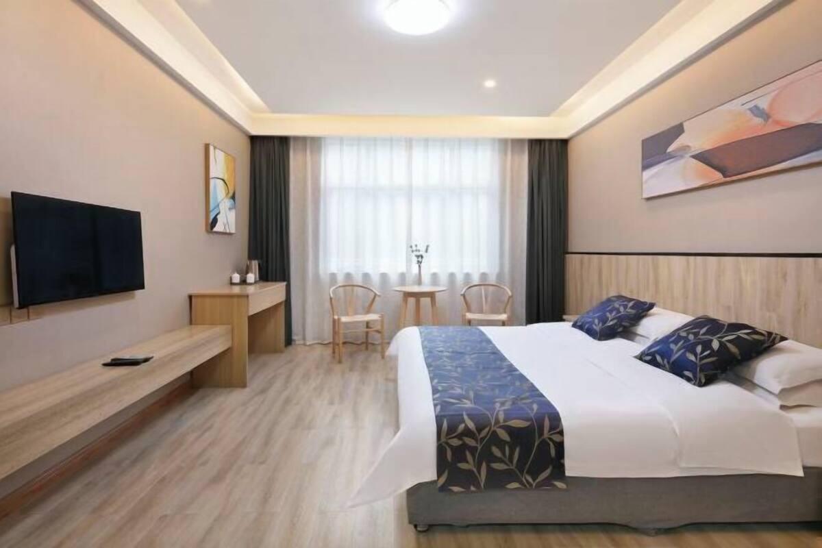 A modern hotel room with a large bed, a TV, a desk, and a window with curtains.