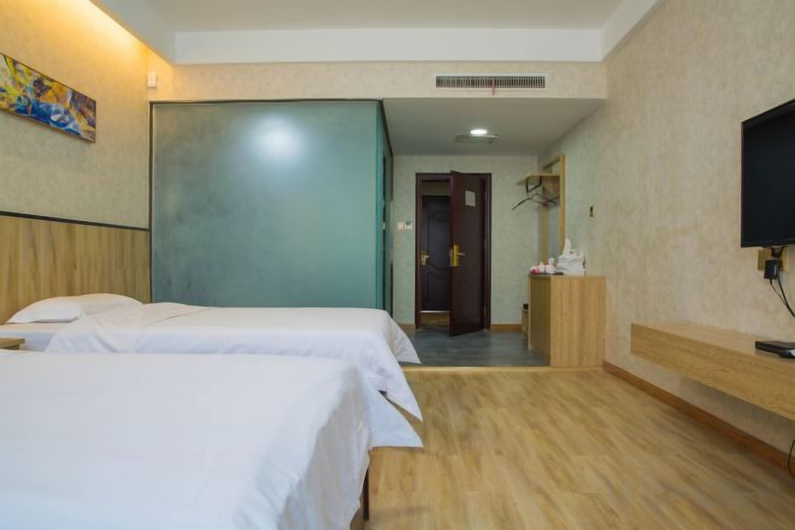 A hotel room with two beds, a wooden floor, a TV, and a door leading to a hallway.