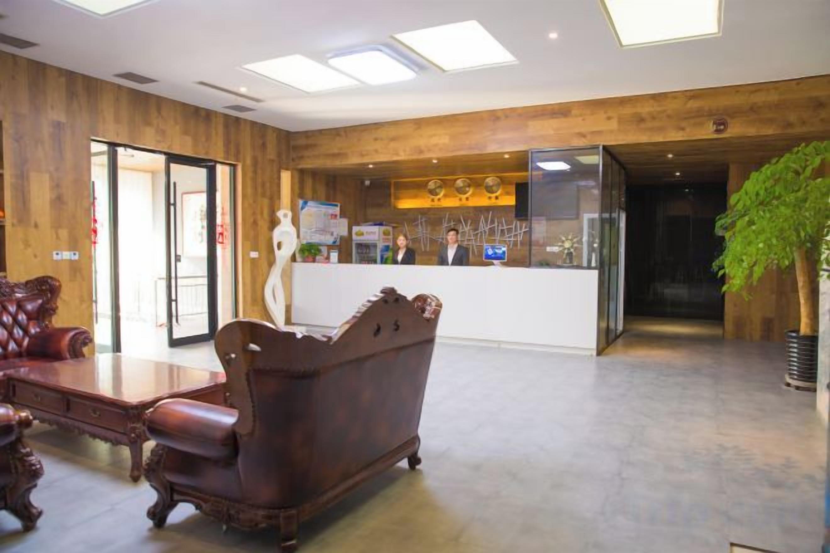 Un área de recepción con un mostrador de madera, sillones de cuero y una gran planta en maceta.