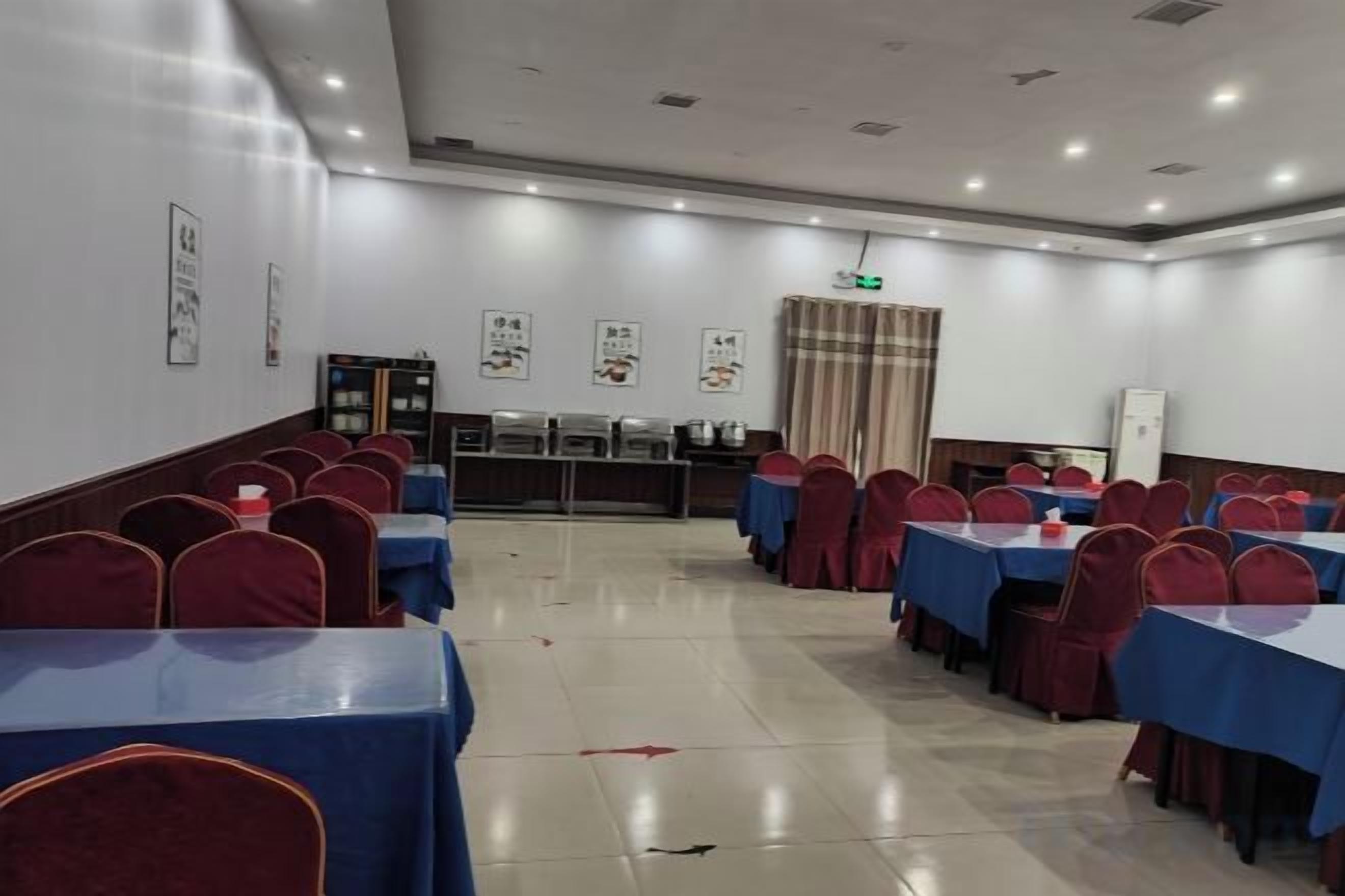 Un salón de conferencias con mesas y sillas dispuestas en filas, una zona de buffet y una pantalla de proyección.