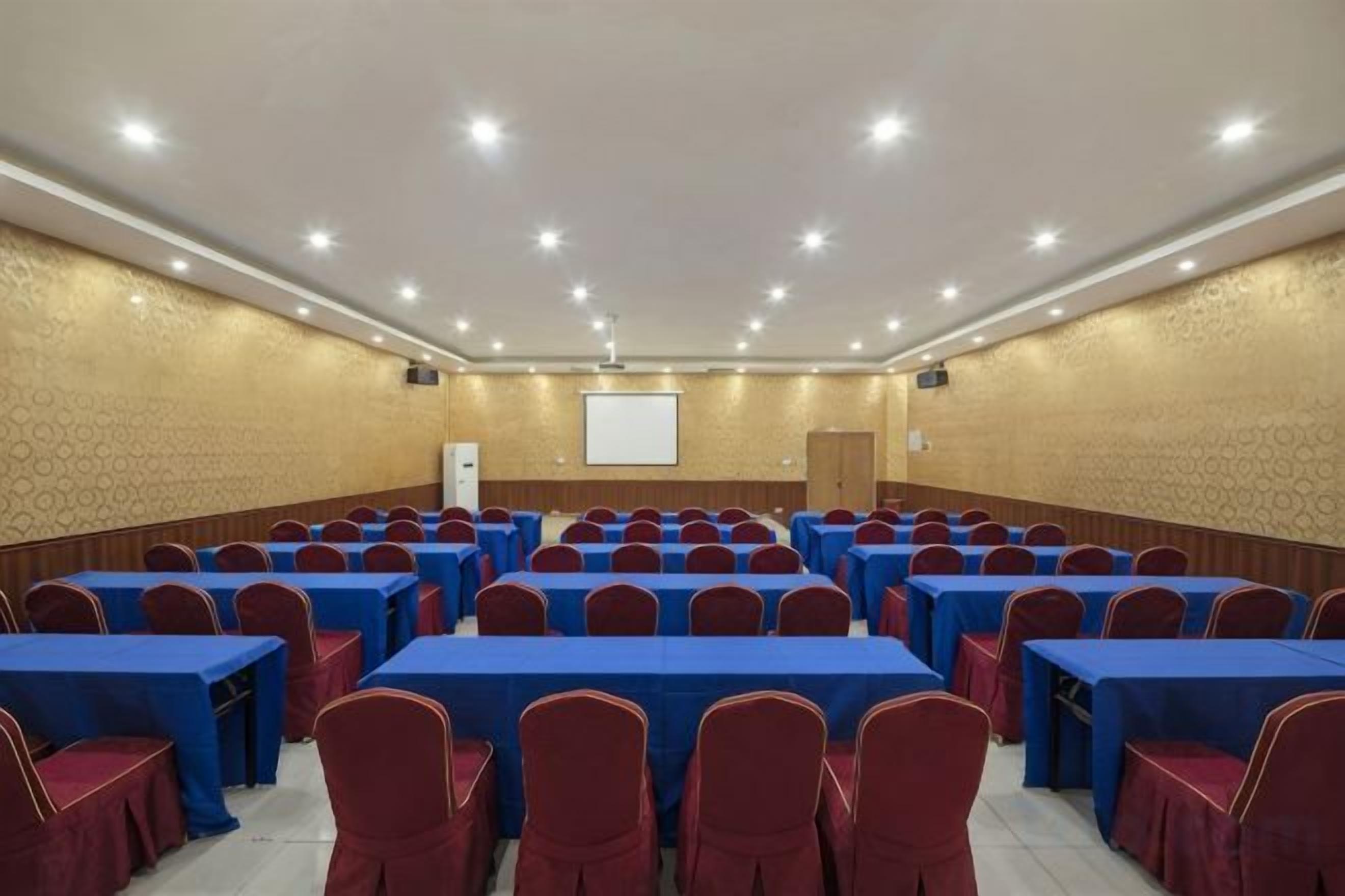 A conference room with rows of tables and chairs, a projector screen, and a door.
