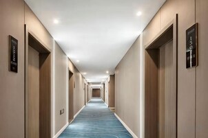 A hotel corridor with doors on both sides, a blue carpet, and ceiling lights.