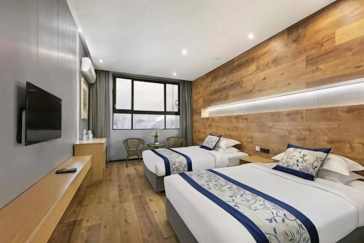 A hotel room with two beds, a TV, a desk, and a window with a view.