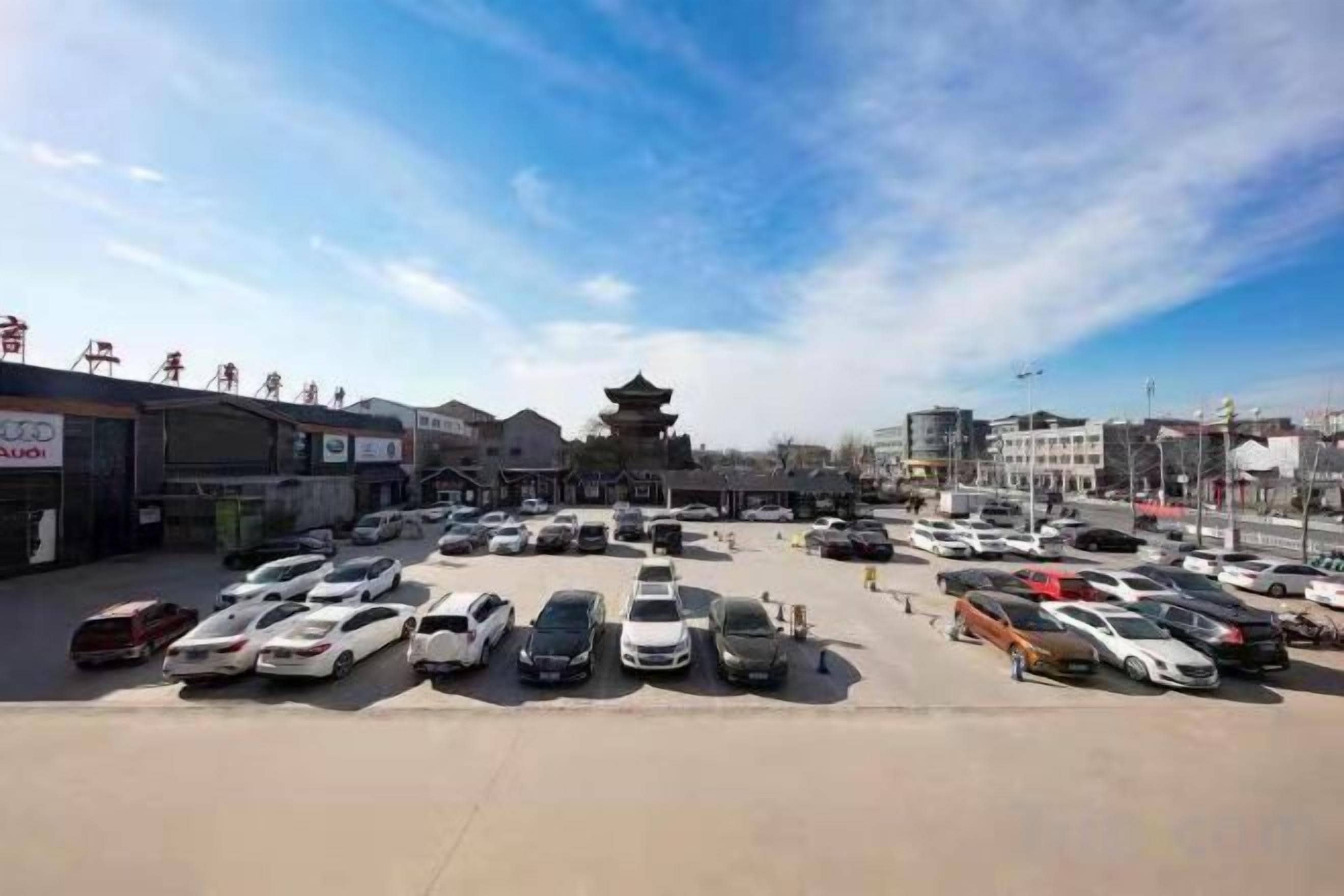 Un parcheggio con diverse automobili e una struttura simile a un pagode sullo sfondo.