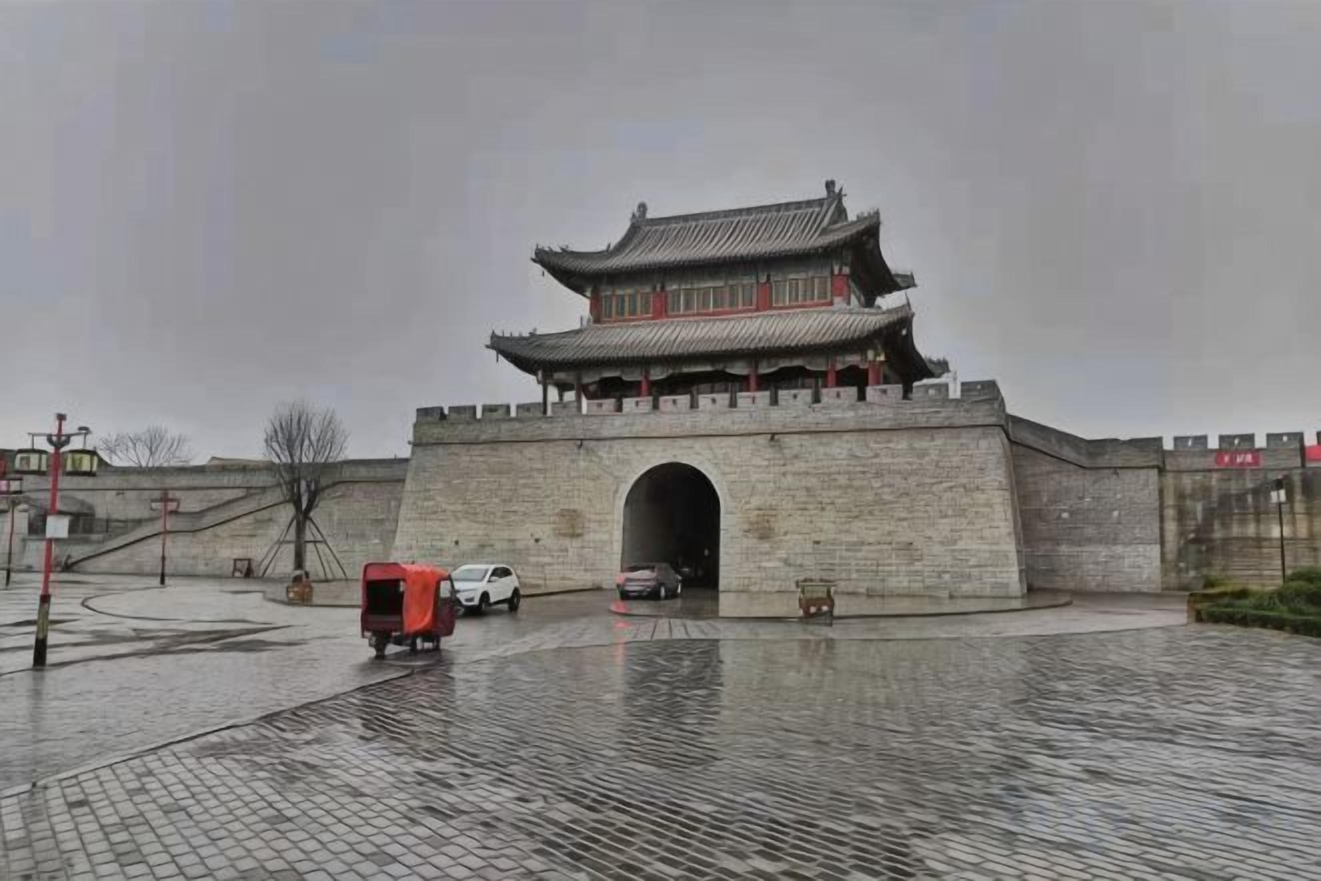 A traditional building with a large archway entrance, a paved courtyard, and a red vehicle parked nearby.