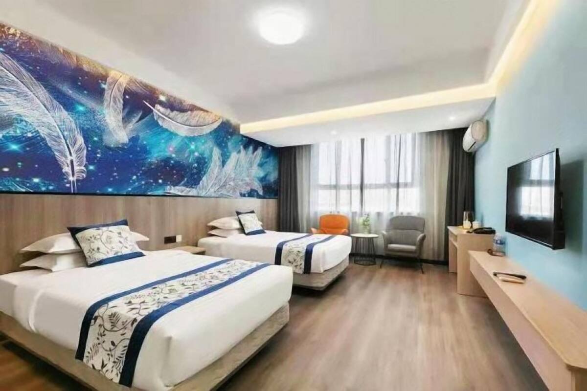 A hotel room with two beds, a desk, a chair, a TV, and a large wall mural.