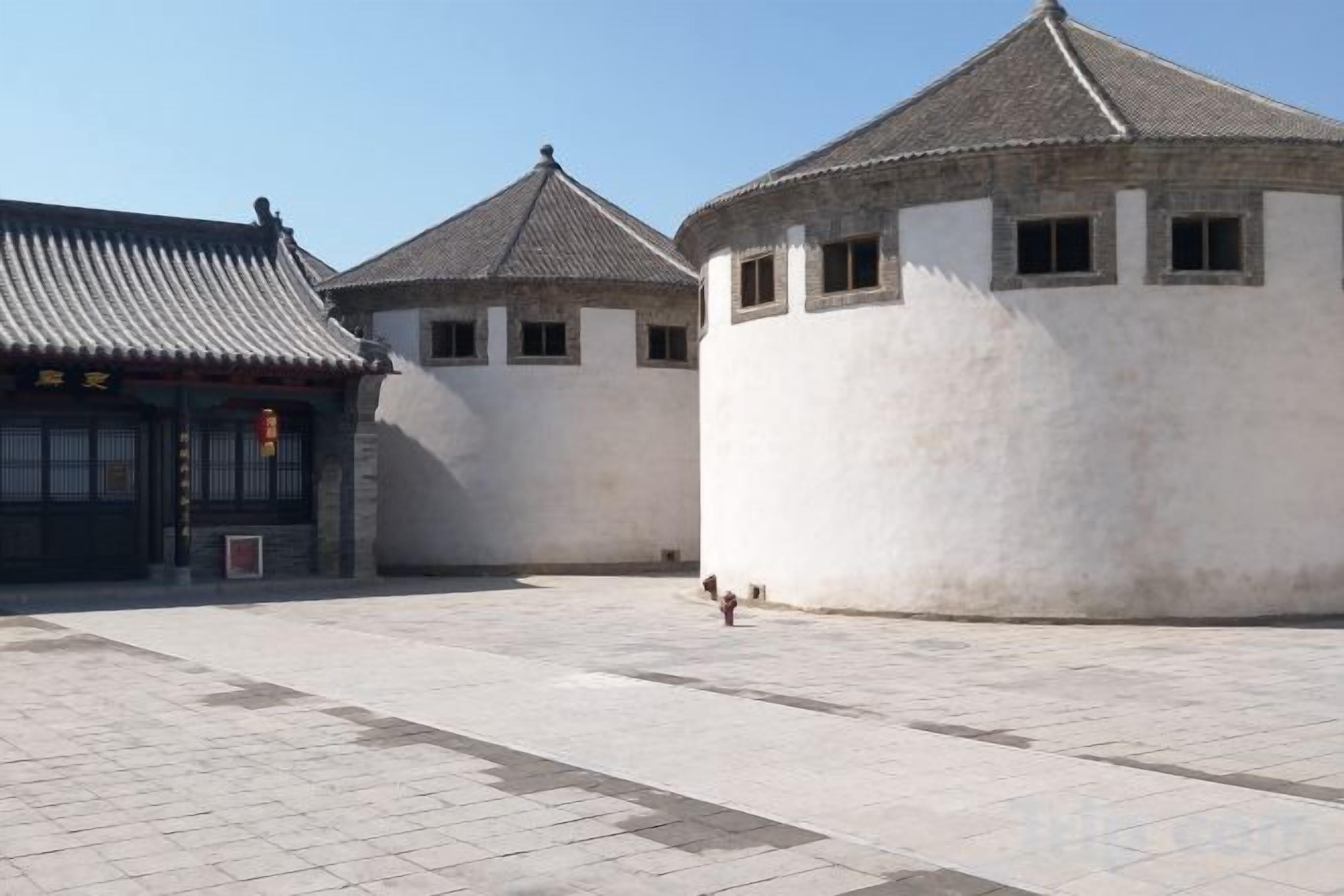 A courtyard with traditional architecture, including a building with a tiled roof and another with a rounded corner.