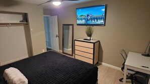 A bedroom with a bed, a desk, a chair, a dresser, a ceiling fan, and a TV on the wall. - Modern/Retro 1br Condo by Exceptional Stays (High Point)