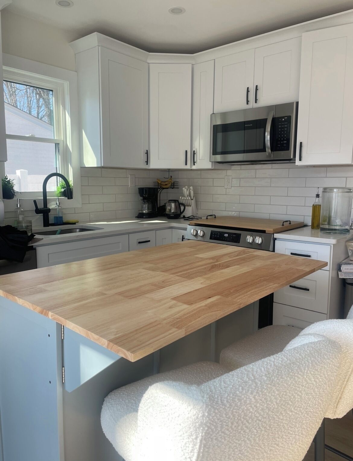 A modern kitchen with white cabinets, a wooden island, a built-in microwave, and a sink with a faucet.