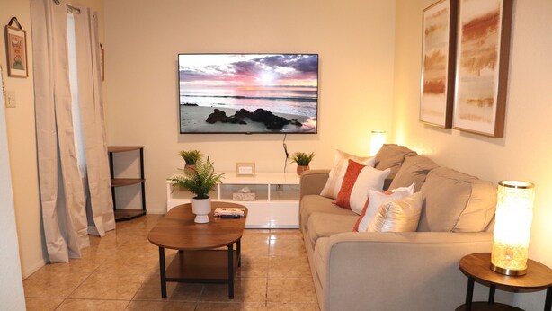 A living room with a TV mounted on the wall, a sofa, a coffee table, and a side table with a lamp.
