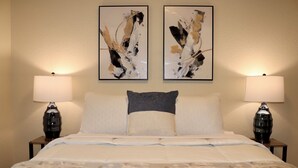 A neatly made bed with a patterned bedspread, two bedside lamps, and two abstract paintings on the wall.