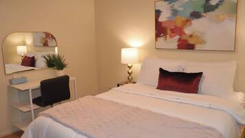 Habitación de hotel con cama, escritorio, silla, lámpara, espejo y un cuadro en la pared.