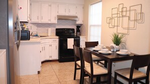 A compact kitchen with white cabinets, a black stove, and a dining table with chairs.