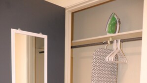 A hallway with a mirror, a hanging ironing board, and a door leading to another room.