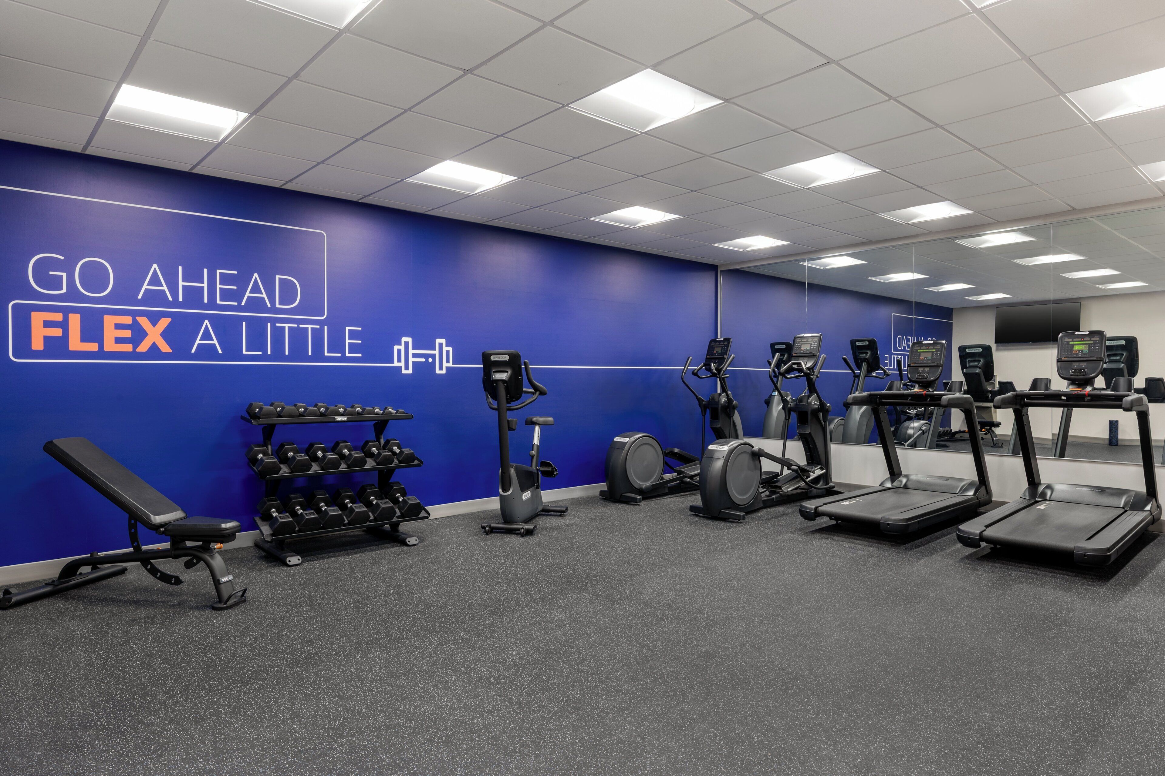 Une salle de sport dotée d’un mur d’inspiration, de tapis de course, d’appareils de musculation elliptique et de poids libres.