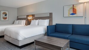 Una camera d'albergo con due letti, un divano blu, un tavolino in legno e opere d'arte alle pareti.