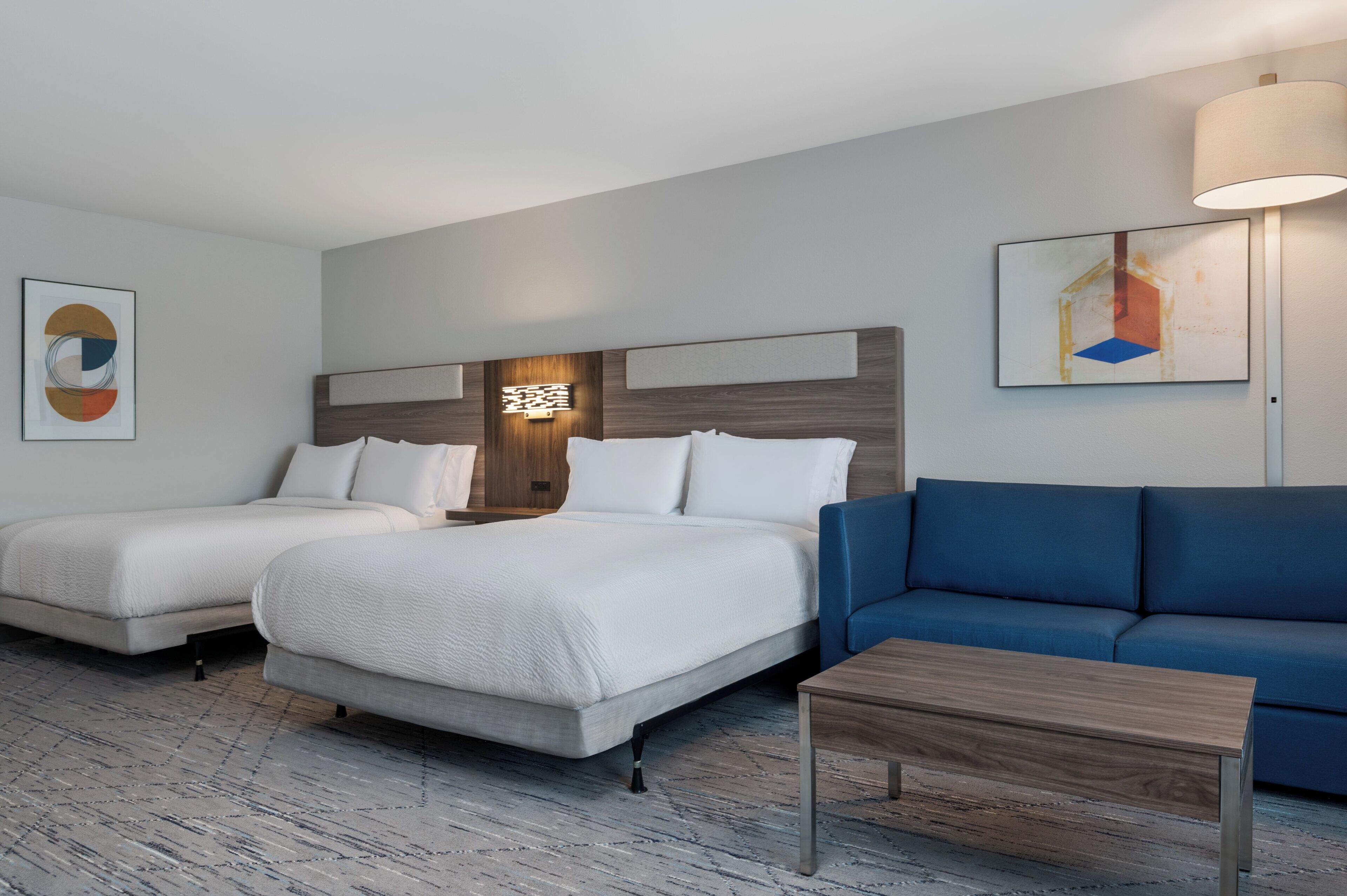 A hotel room with two beds, a blue sofa, and a wooden coffee table.