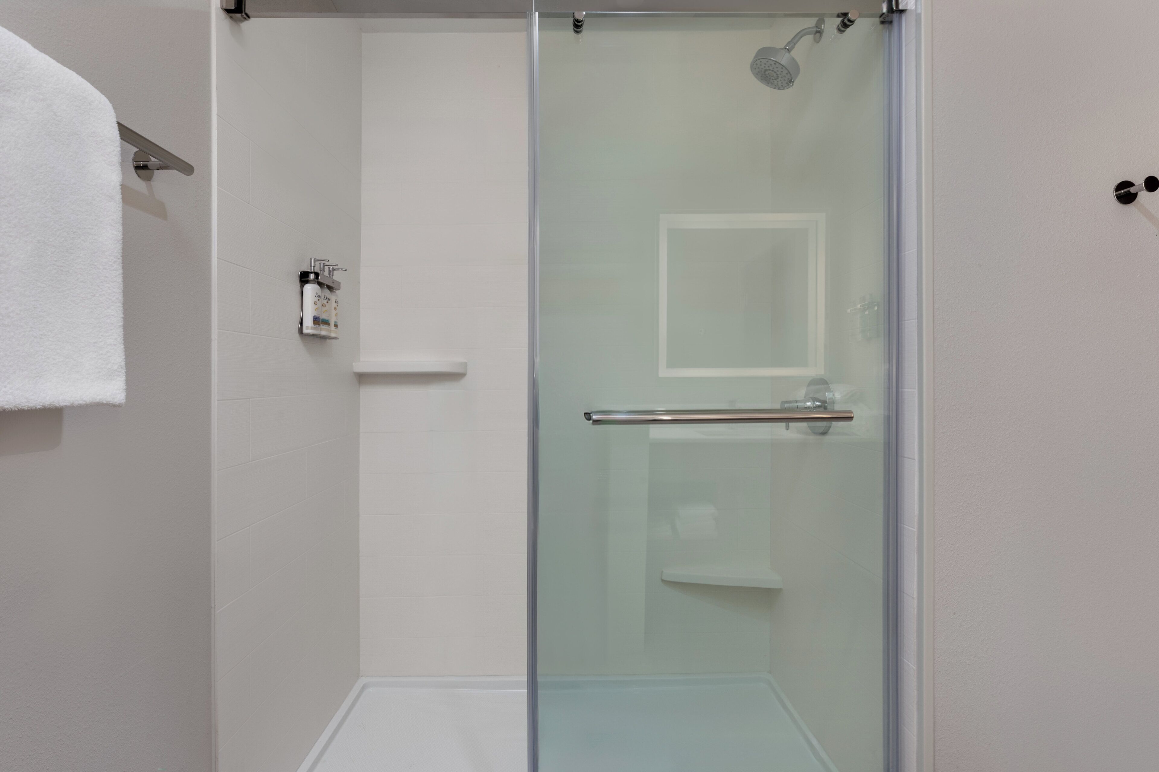 A modern bathroom with a glass shower enclosure, a white towel hanging on a rack, and a small shelf with toiletries.