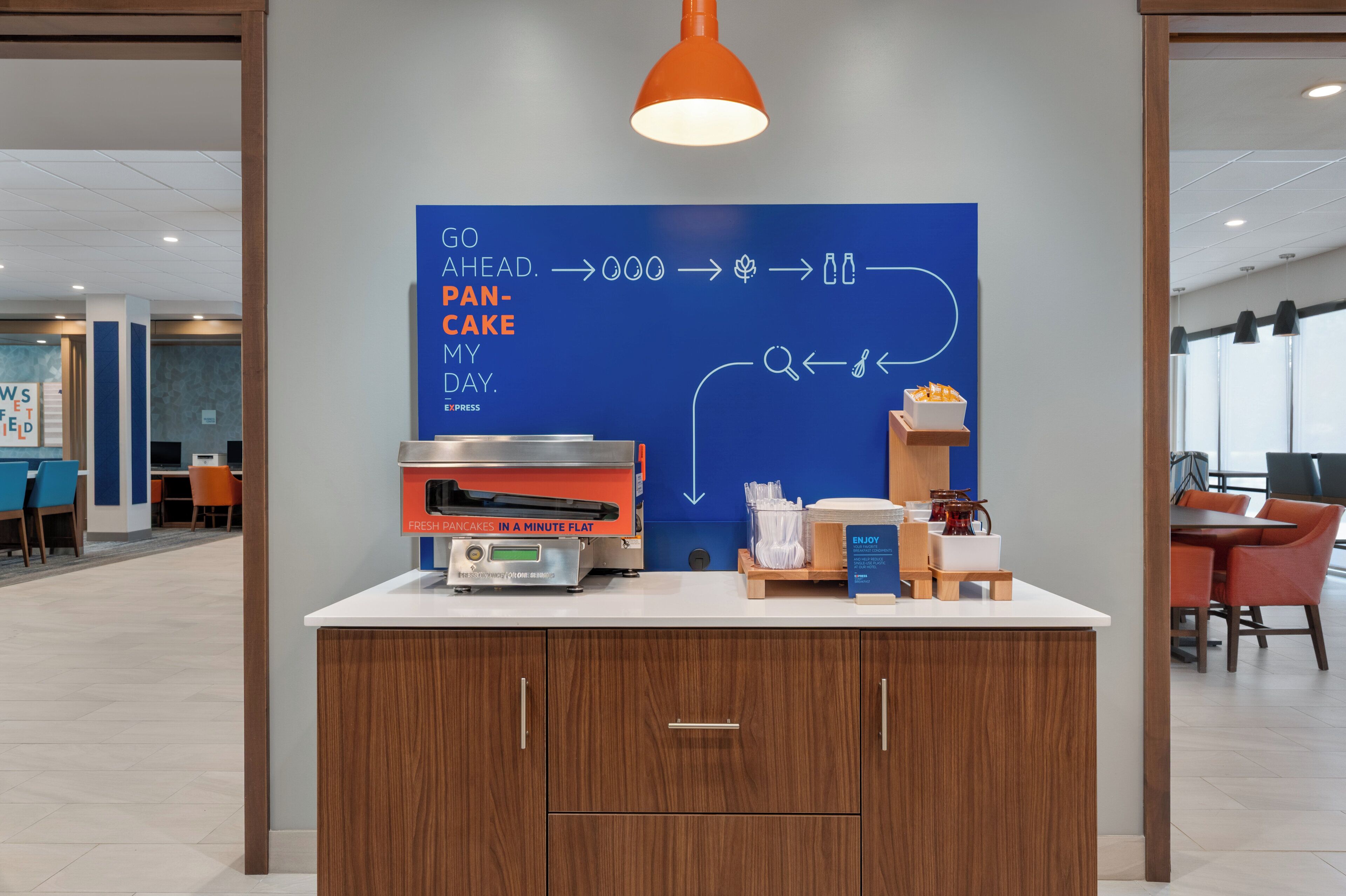 A modern kitchen area with a flat-screen TV, a coffee machine, and a sign that reads "GO AHEAD. PANCAKE MY DAY."
