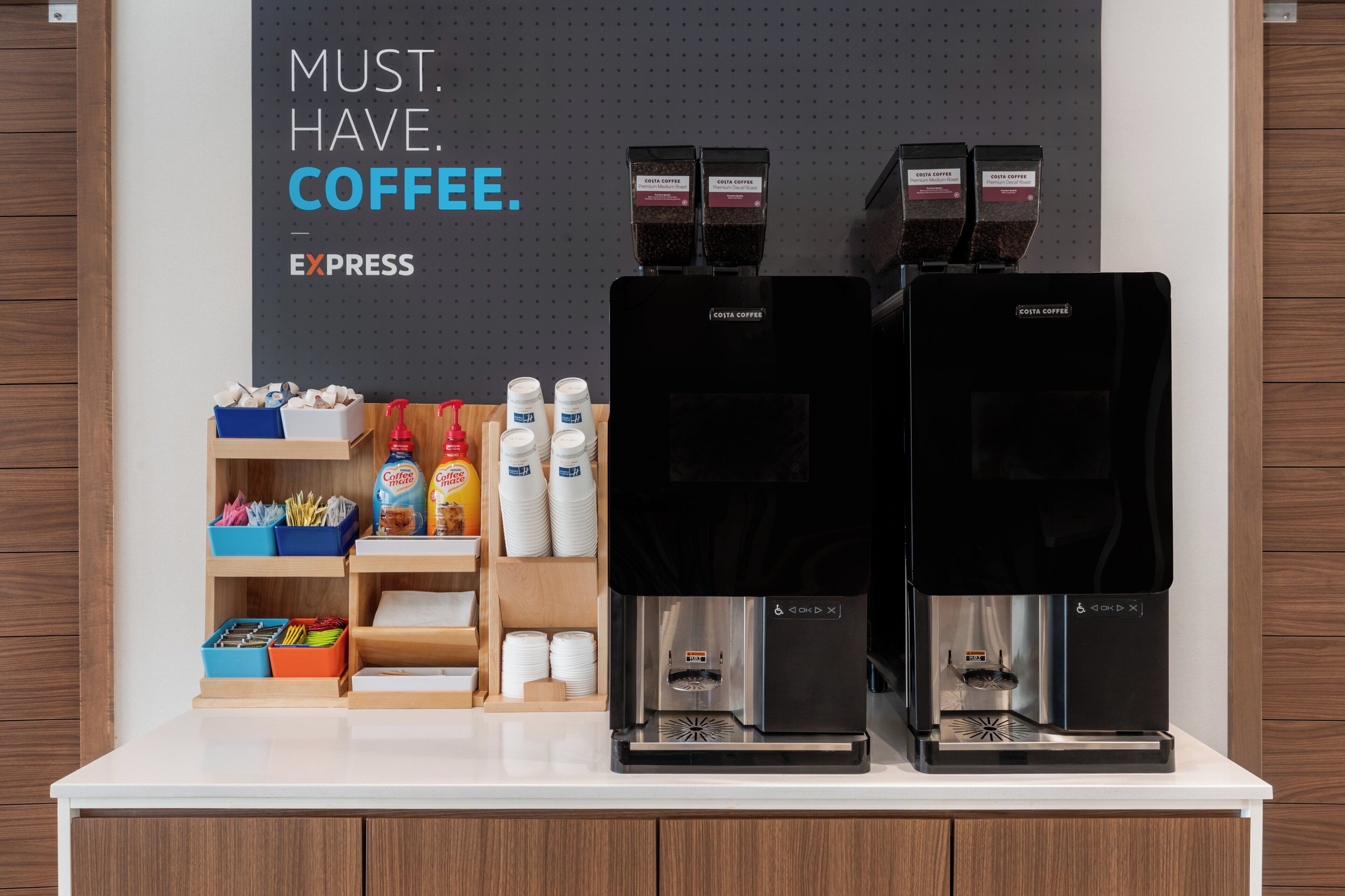 Two coffee machines on a counter with coffee pods, cups, and a sign that reads "MUST. HAVE. COFFEE."