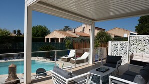 Ein überdachter Außenbereich mit Pool, Liegestühlen und einem Tisch.