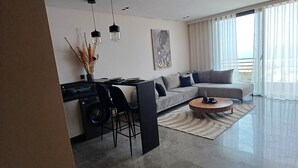 Ett modernt vardagsrum med en grå soffa, en matplats med bord och stolar samt ett köksområde med tvättmaskin.