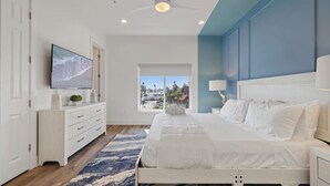 Un dormitorio moderno con cama, cómoda, televisor y ventana con vista a la ciudad.
